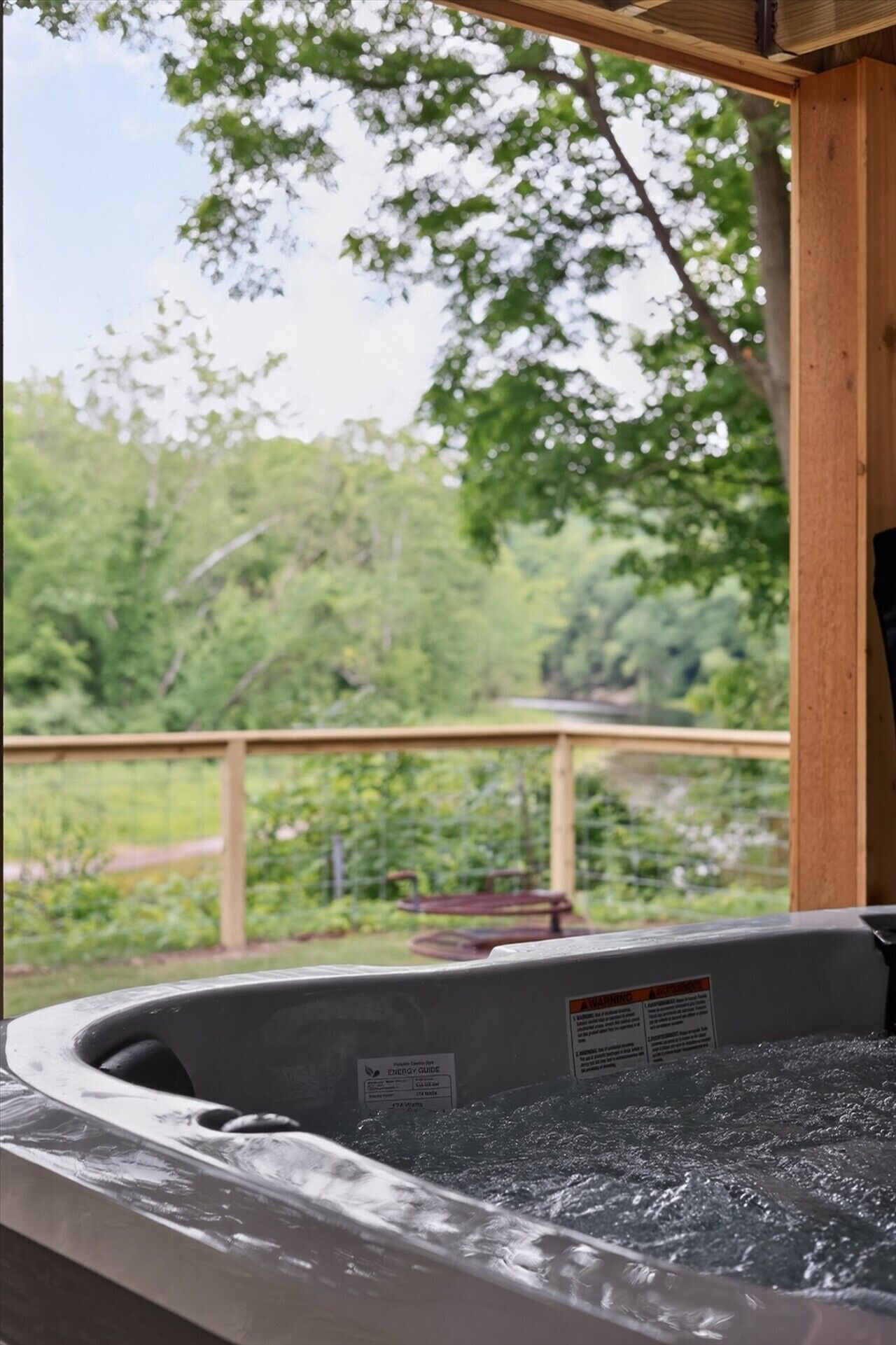 A hot tub with an ENERGY GUIDE label, surrounded by a wooden deck and a view of greenery.