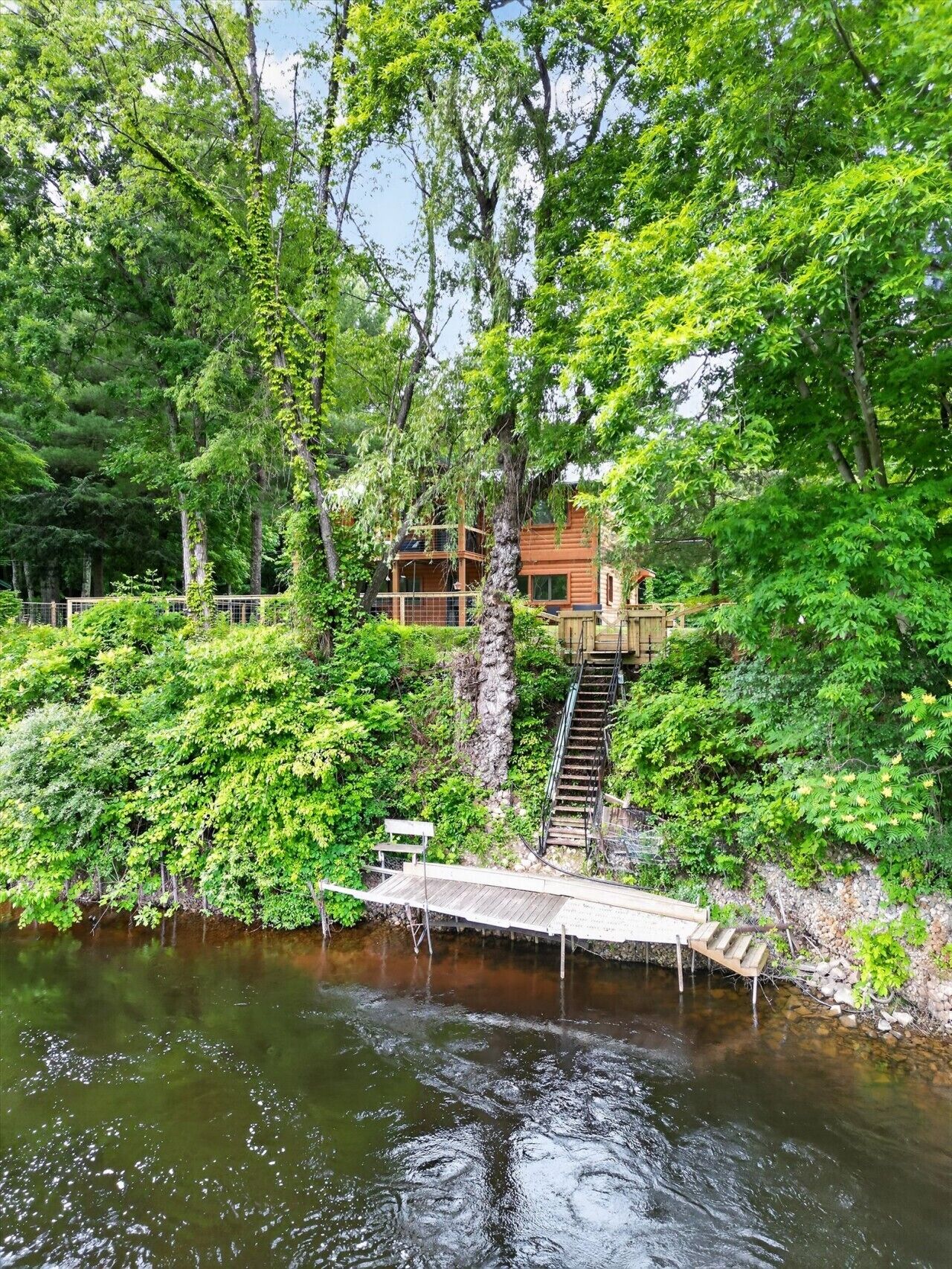 A wooden cabin with a staircase leading to a deck over a river.
