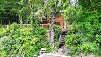 A wooden cabin with a staircase leading to a deck over a river.