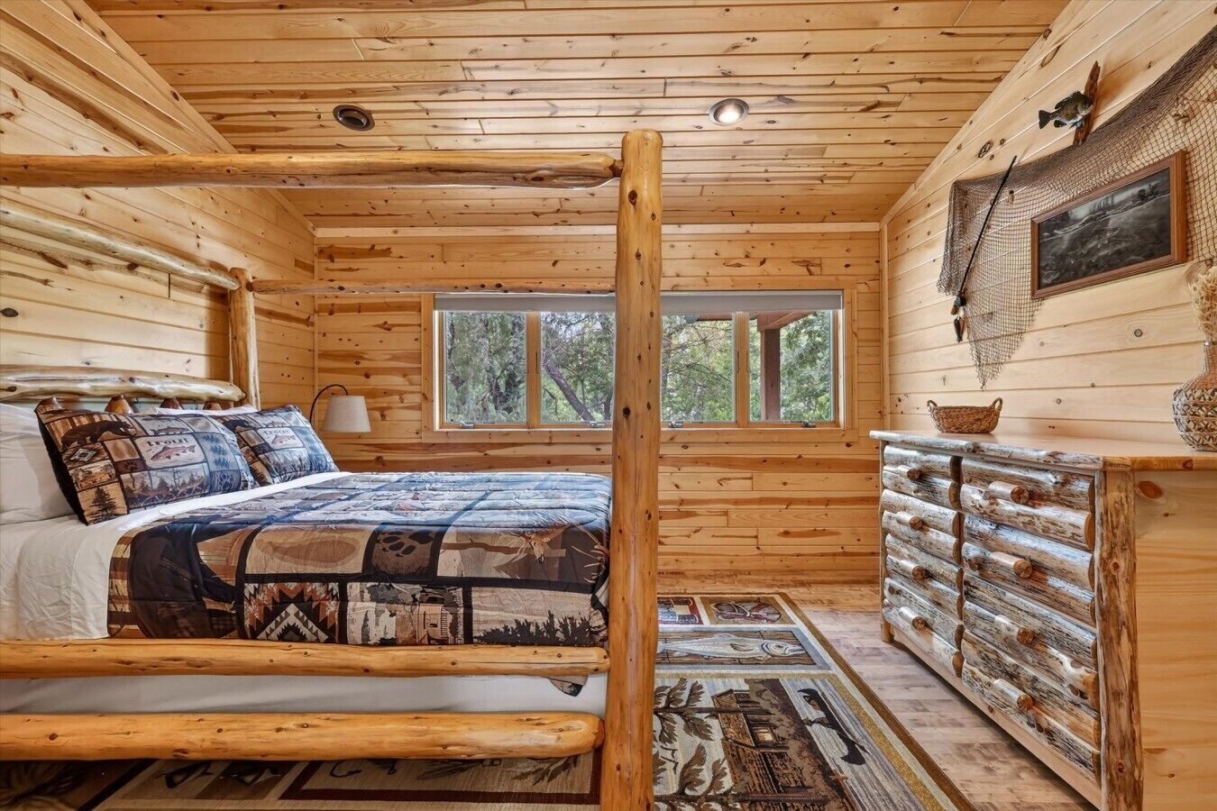 A log cabin bedroom with a bed, a dresser, a window, and a ceiling light.