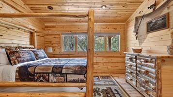 A log cabin bedroom with a bed, a dresser, a window, and a ceiling light.