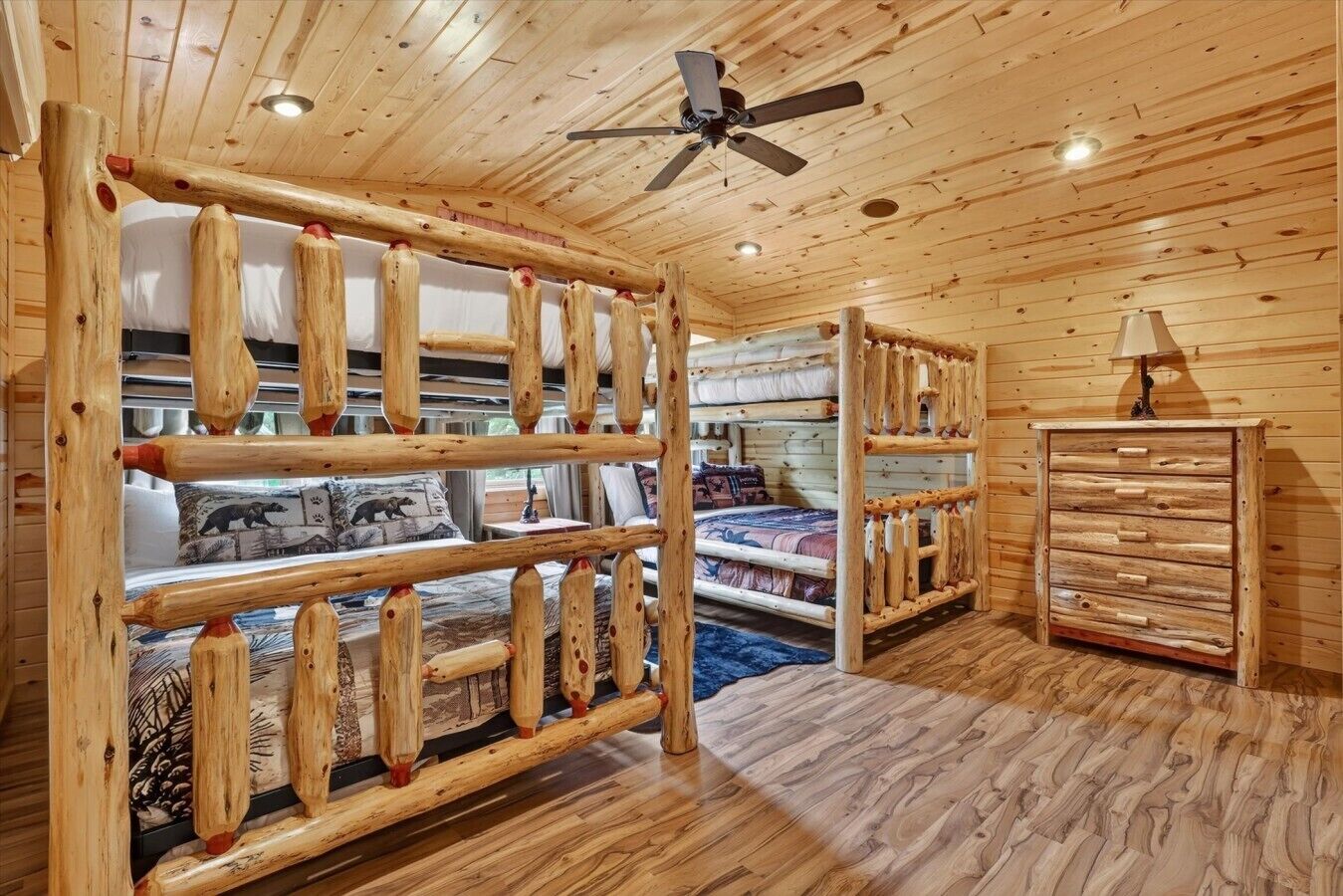 A cabin interior with a bunk bed, wooden walls, a ceiling fan, and a dresser.