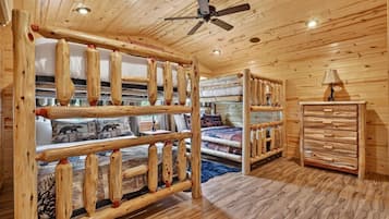 A cabin interior with a bunk bed, wooden walls, a ceiling fan, and a dresser.