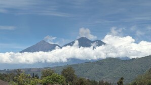 A mountain landscape with two prominent peaks, a forested valley, and a partly cloudy sky. - Casa de Huéspedes Elizabeth (Antigua Guatemala)