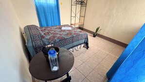 A bedroom with a bed, a small table with a water bottle, a chair, a potted plant, and a blue curtain. - Casa de Huéspedes Elizabeth (Antigua Guatemala)