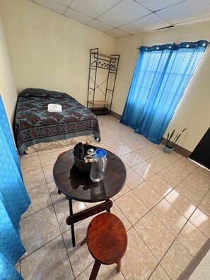 Una habitación con una cama, una mesita y una botella de agua, además de una cortina azul.
