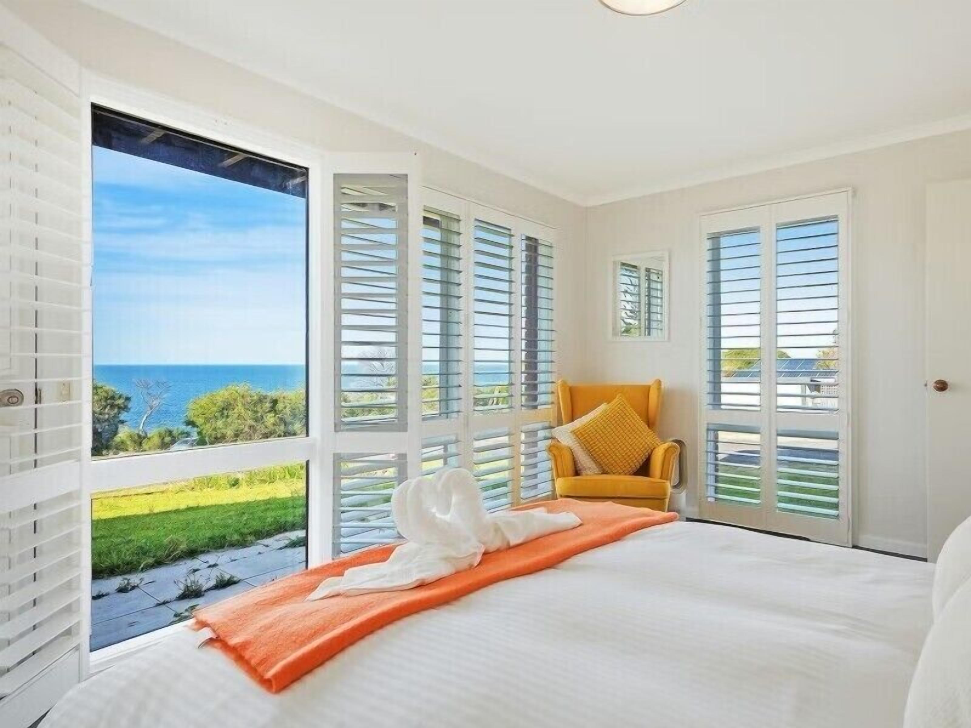 A bedroom with a bed, a chair, and a view of the sea.