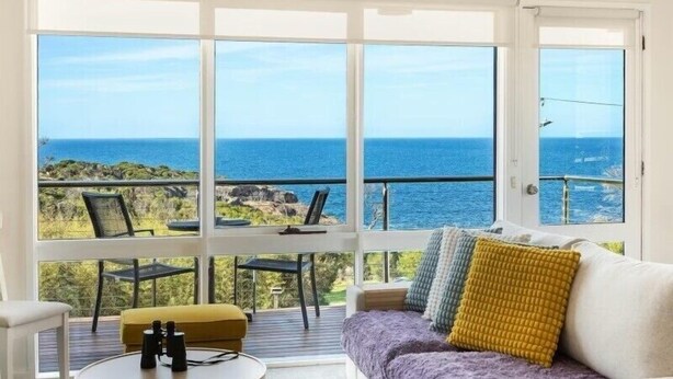 Una stanza con una grande finestra vista mare, un divano con cuscini, un tavolino con binocolo e una poltrona.