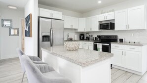 A modern kitchen with white cabinets, a stainless steel refrigerator, a microwave, and a granite countertop island. - Spacious 4-bedroom house  with AC  15 minutes from Miami airport/ 14 ppl (Miami)