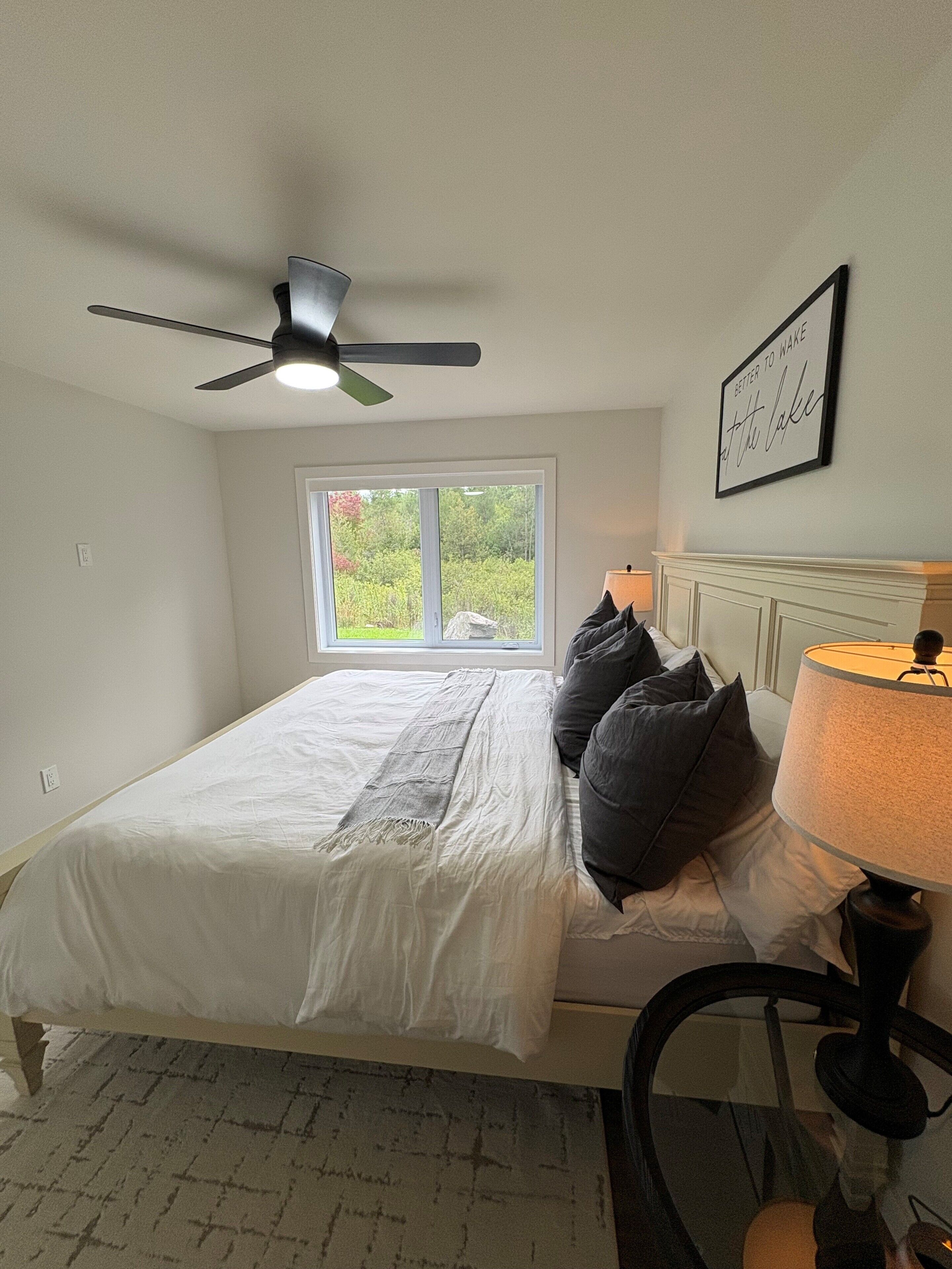 Une chambre à coucher avec un lit, un ventilateur de plafond, une fenêtre, une lampe de chevet et une citation encadrée accrochée au mur.