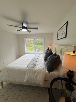 A bedroom with a bed, a ceiling fan, a window, a bedside lamp, and a framed quote on the wall.