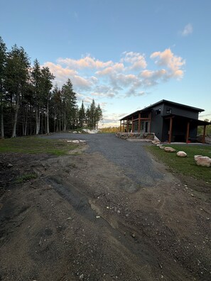 A gravel driveway leading to a modern building with a covered porch area, surrounded by a forested landscape.