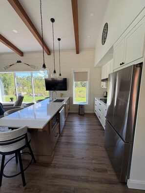 A modern kitchen with a large island, stainless steel appliances, and a view of greenery outside.