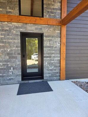 A modern building entrance with a stone facade, a wooden beam structure, and a clear view into the driveway.