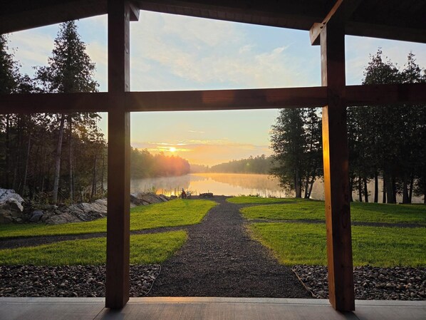 A covered outdoor area with a view of a lake and forest.