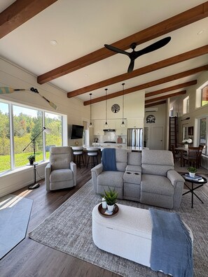 A spacious living room with a large gray sectional sofa, a white ottoman, and a ceiling fan.