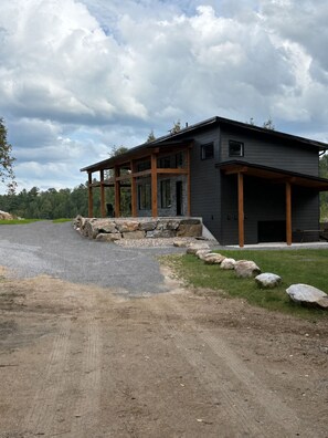 A modern two-story house with a covered porch and a stone retaining wall.