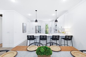 Een moderne keuken met witte kasten, zwarte stoelen en hanglampen.