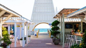Un paseo marítimo que lleva a un restaurante con terraza, vistas al mar y un edificio alto al fondo.