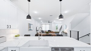 Una cocina moderna con una isla grande, armarios blancos e iluminación colgante.
