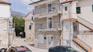 A two-story stone building with a balcony, a staircase, and a car parked in front. - B Studio Apartment Near the Beach With sea View (Kastela)