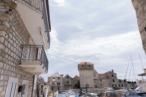 Ein historisches Steinhaus mit einem Turm, einer schmalen Gasse und geparkten Autos.
