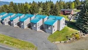 A row of modern, single-story buildings with blue roofs, surrounded by a forested area and a mountain in the background. - ​5-Min Walk to Lake! Spacious 5BR Condo w/ Fire Pits (Cascade)