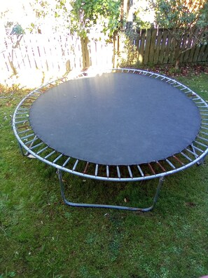 En rund trampolin med ett skyddsnät, placerad på en gräsplätt.