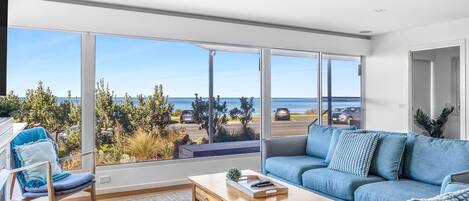 A spacious living room with a large sliding glass door leading to a parking area and a view of the sea.