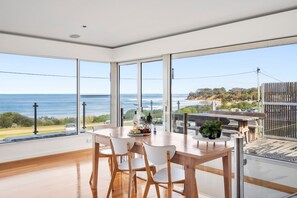 A dining area with a wooden table and chairs, large windows with a view of the sea and a distant landscape. - Front Row Seats on the Esplanade (Torquay)