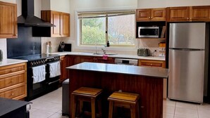 A kitchen with wooden cabinets, a black stove, a stainless steel refrigerator, and a window with a view of greenery.