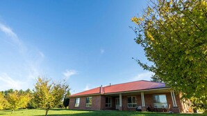 A single-story brick house with a red roof, a front porch, and a lawn.