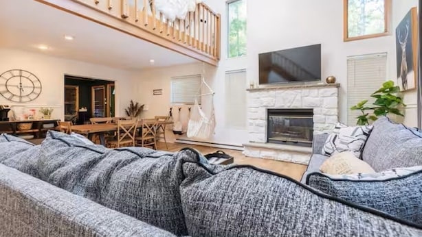 Ein großzügiger Wohnbereich mit hoher Decke, Kamin, Fernseher und einem Balkon mit Geländer.
