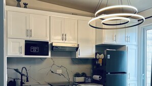 Una cucina moderna con mobili bianchi, un piano cottura nero, un frigorifero e un originale lampadario a forma circolare.