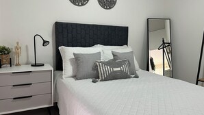 Una camera da letto con un letto, una cassettiera, una lampada, due decorazioni a parete e uno specchio.