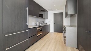 Une cuisine moderne avec des meubles de couleur sombre, un four à micro-ondes encastré et un petit îlot central doté de tabourets de bar.