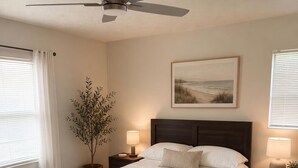 A bedroom with a bed, nightstands, a ceiling fan, a window with blinds, a plant, and a painting on the wall. - Serene 3-bedroom 2 bathroom house with  pool and dining area-pet friendly (Lake Placid)