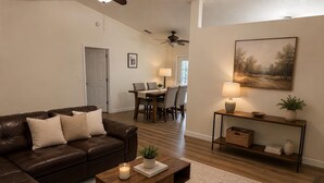 A living room with a brown leather couch, a wooden coffee table, a rug, a painting on the wall, and a dining area in the background. - Serene 3-bedroom 2 bathroom house with  pool and dining area-pet friendly (Lake Placid)