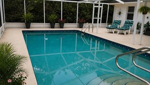 A covered swimming pool with a glass floor, surrounded by potted plants and lounge chairs. - Serene 3-bedroom 2 bathroom house with  pool and dining area-pet friendly (Lake Placid)