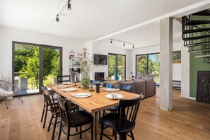 Uma área de refeições moderna com uma mesa de madeira, cadeiras pretas e vista para o verde lá fora.