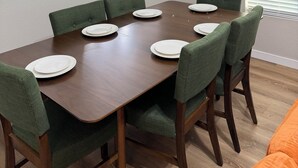En spisestue med et rektangulært bord, seks stole, en lysekrone og et vindue med skodder.