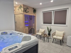 Une salle de bain moderne avec un jacuzzi, un lambris en bois, une douche en verre et deux fauteuils en osier.