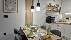 Une cuisine moderne avec une table à manger en bois, des chaises, une machine à café et un luminaire suspendu.