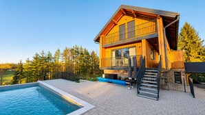 Una casa a due piani in legno con piscina, scale esterne e vista su una zona boschiva.
