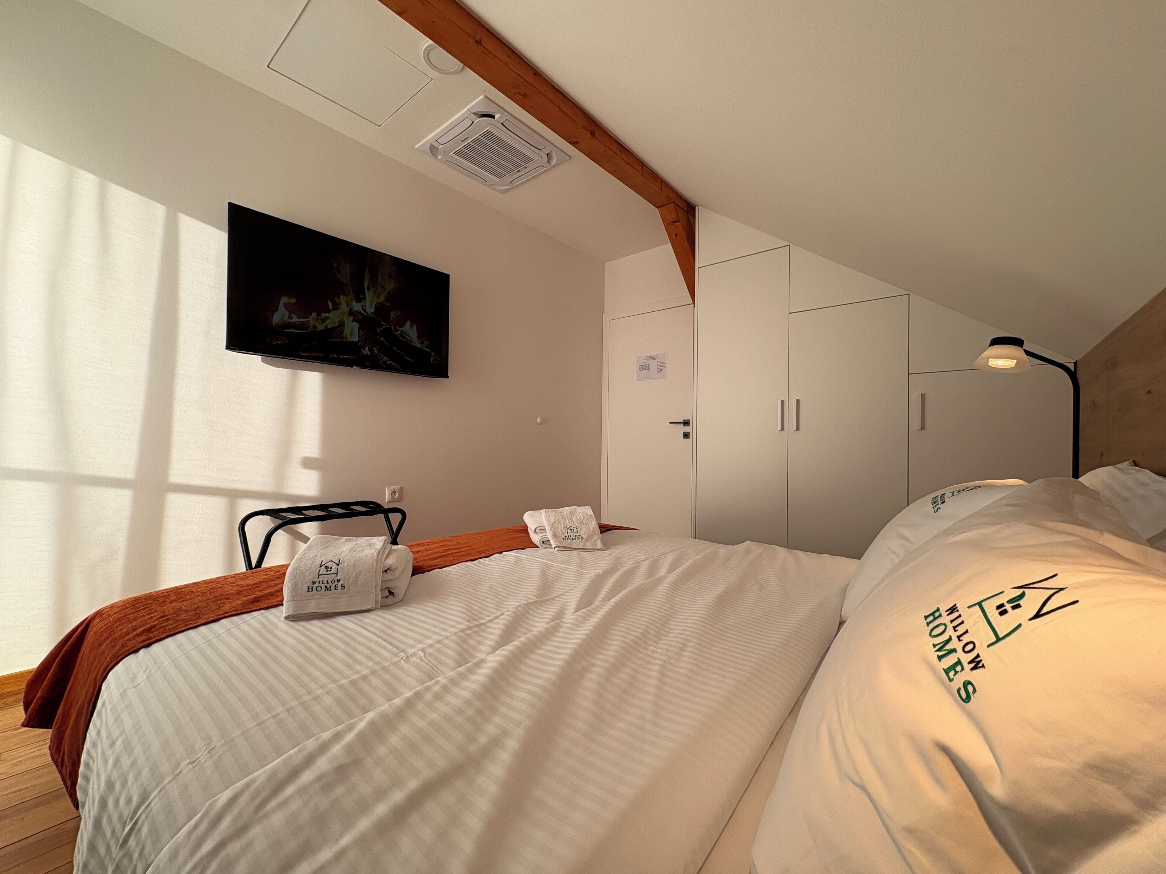 Una habitación de hotel con cama, televisión montada en la pared, armario y rejilla en el techo.