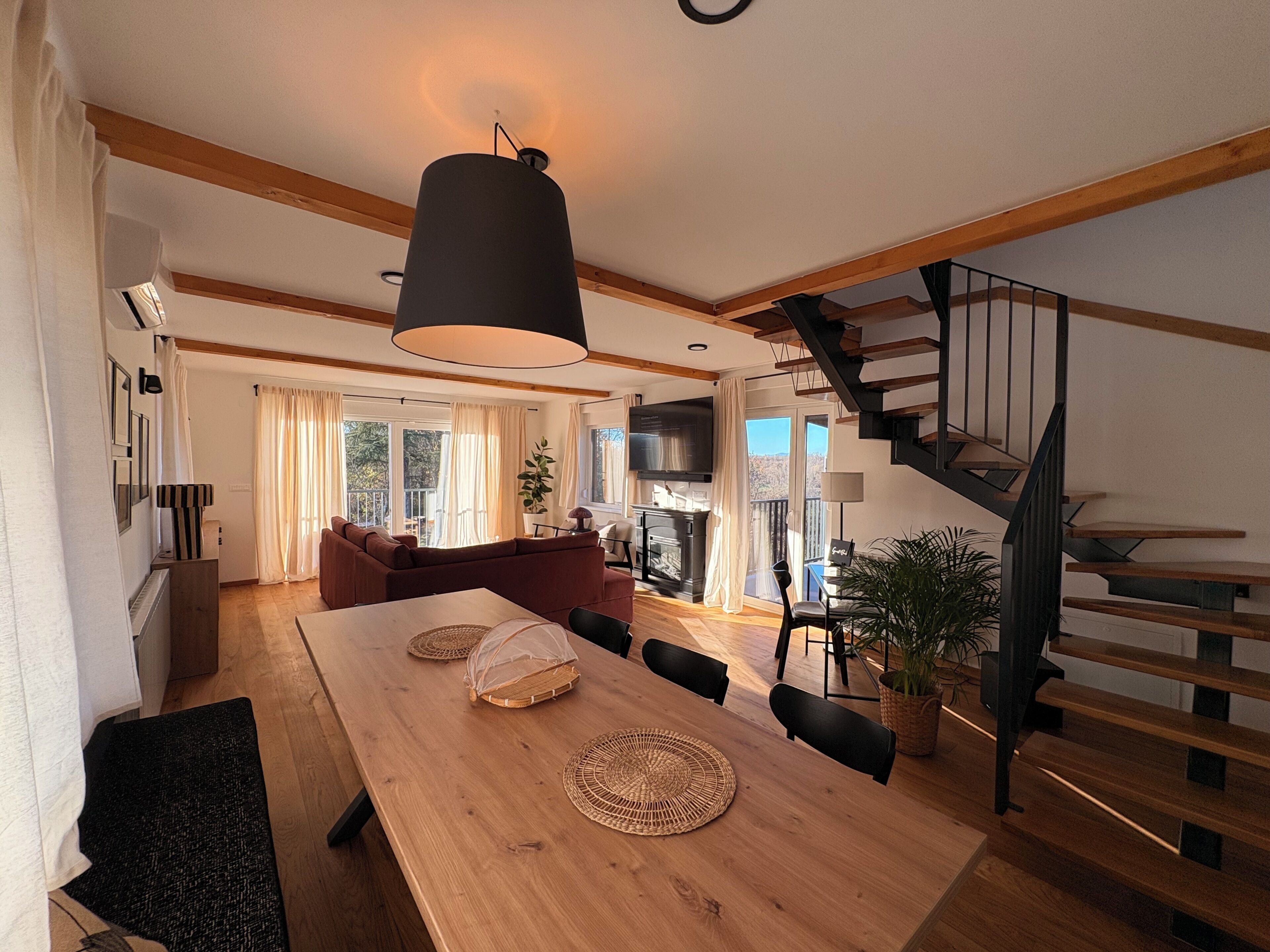 A spacious living area with a wooden dining table, a sofa, and a staircase.