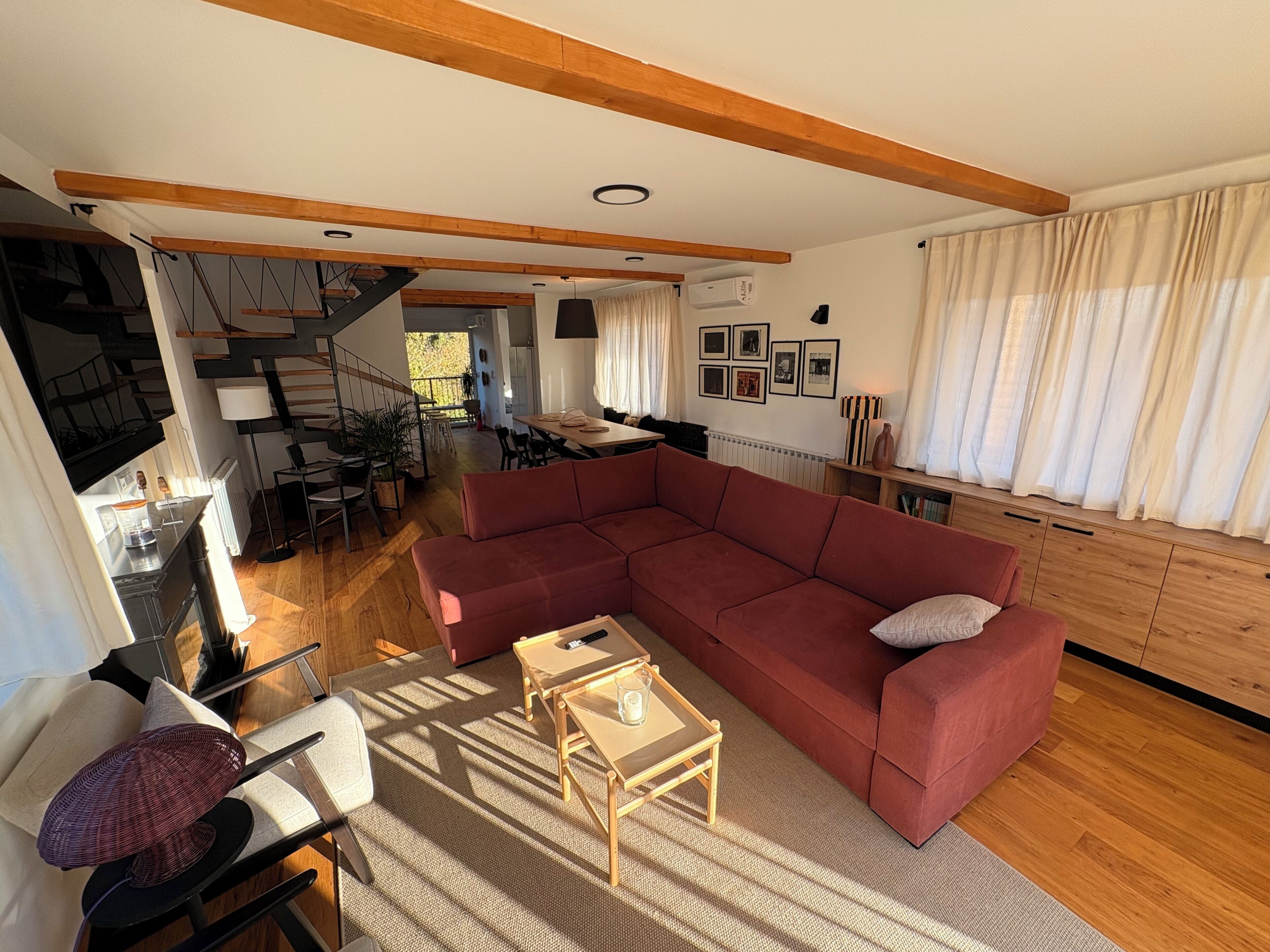 A modern living room with a large red sectional sofa, a small wooden table, and a dining area with a staircase.