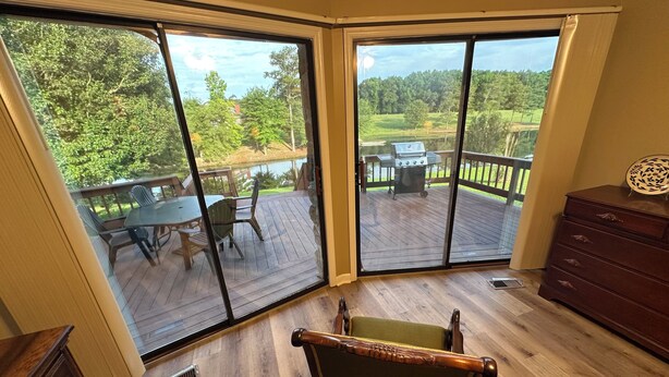 A room with a sliding glass door leading to an outdoor deck with a table and chairs, a grill, and a view of a wooded area. - Cozy Short Creek Cottage in welcoming Boaz with 2 BR AC for relaxing stays (Boaz)