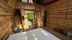 A wooden cabin room with a bed, a chair, a ladder, and a window overlooking greenery. - Cozy Short Creek Cottage in welcoming Boaz with 2 BR AC for relaxing stays (Boaz)