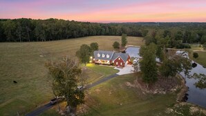 A large house with a driveway, surrounded by a grassy field and a body of water. - Cozy Short Creek Cottage in welcoming Boaz with 2 BR AC for relaxing stays (Boaz)